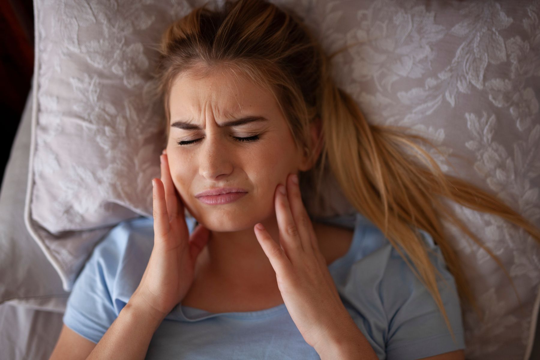 a woman waking in bed touching her jaw in pain