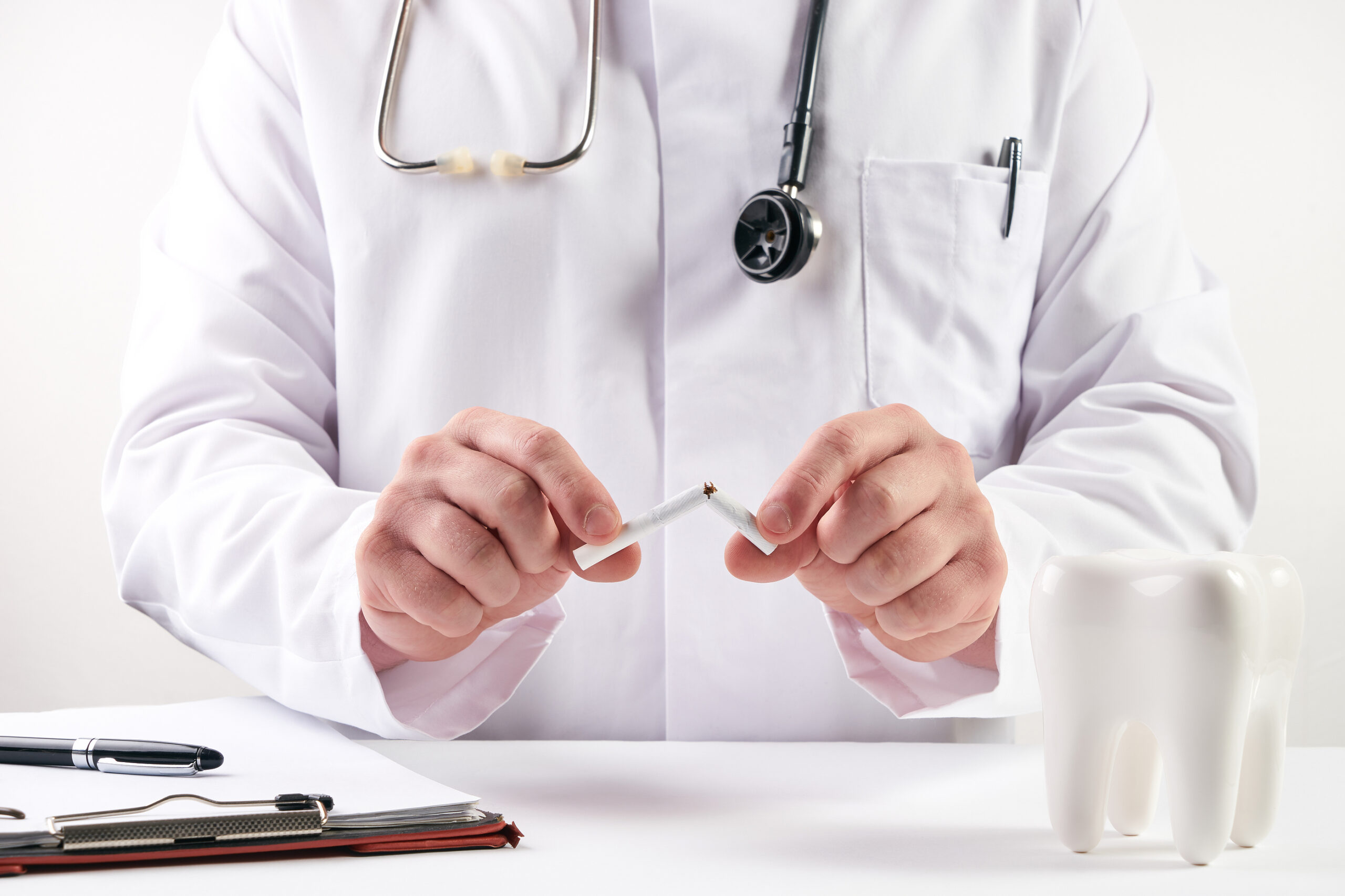 Young doctor dentist in dentist office is breaking cigarette and giving advice to stop smoking. Healthcare and medicine concept